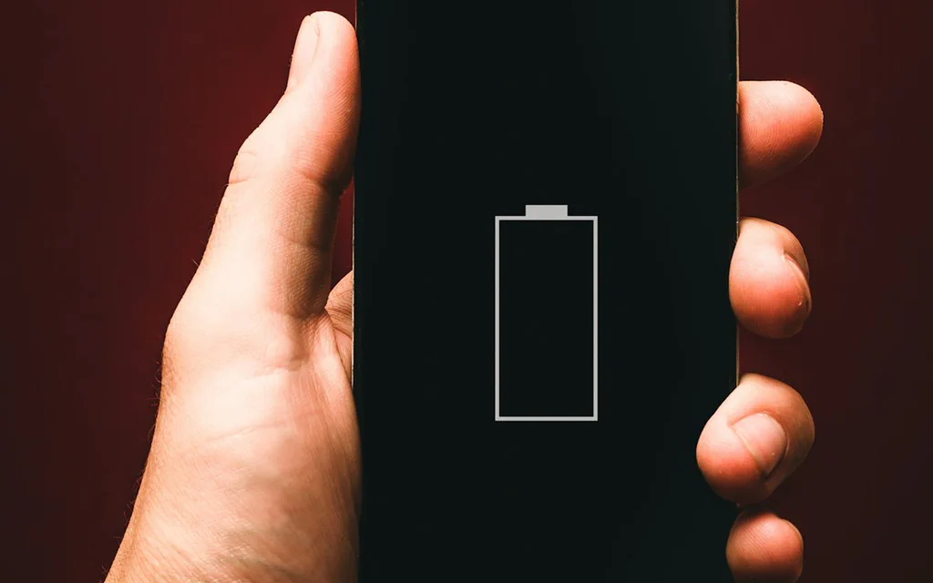 A phone showing an empty battery icon in a user's hand.