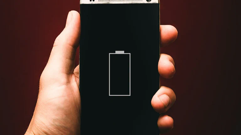A phone showing an empty battery icon in a user's hand.