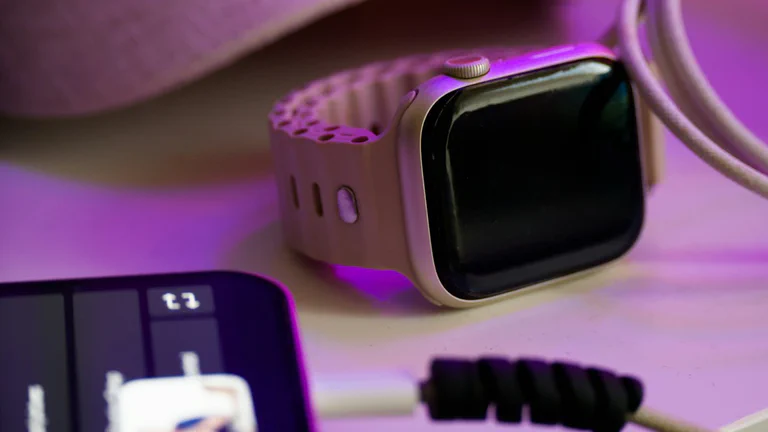 Ein Smartphone, eine Smartwatch und ein Ladekabel auf einem Schreibtisch unter dezentem Licht.