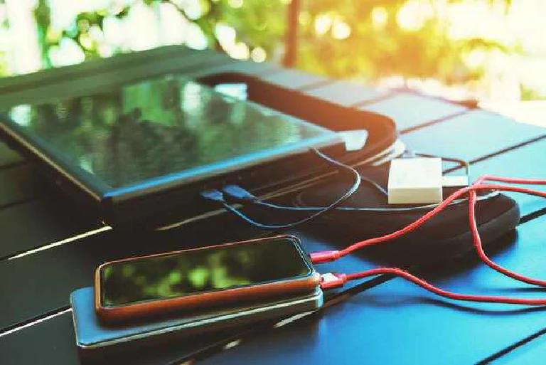 A smartphone displaying a healthy battery icon, with other gadgets like a smartwatch and laptop in the background.