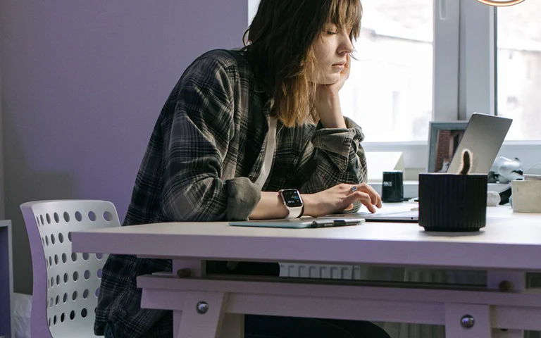 A person working on a thin laptop at a home desk near a window.