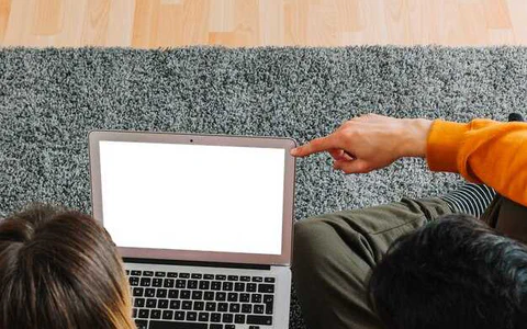 A sleek ultrabook balanced on a scale against a pile of dongles and a larger, thicker laptop.